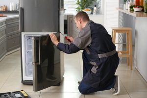 male technician repairing refrigerator in kitchen